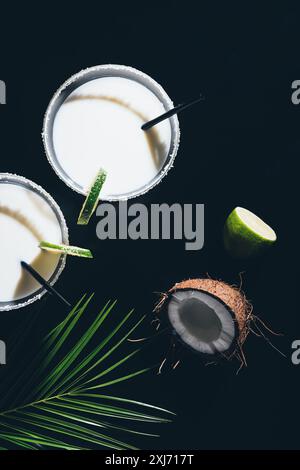 top view of glasses with coconut cocktails and drinking straws, lime and green palm leaves on black Stock Photo