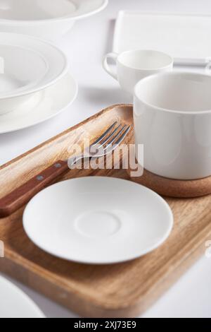 selective focus of wooden tray, fork, various plates, cup and bowl on white table Stock Photo
