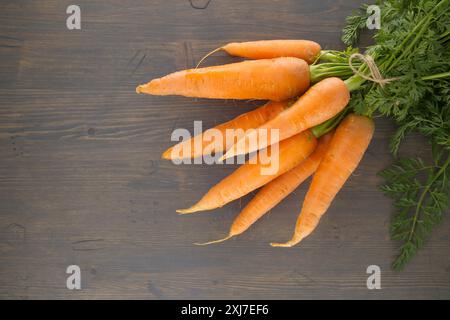 Bunch of fresh, orange carrots with green tops is neatly tied together using twine and positioned on an old, rustic wooden table Stock Photo