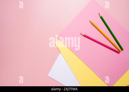 Three pencils are on top of a stack of papers. The pencils are green, yellow, and red Stock Photo