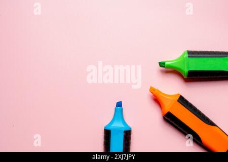 Three markers of different colors are placed on a pink background. The markers are green, blue, and orange. Concept of creativity and organization, as Stock Photo
