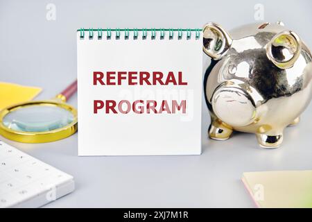 Business concept. Words REFERRAL PROGRAM word on a notepad on a gray background next to a piggy bank, calculator, magnifying glass and stickers Stock Photo