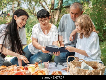 Family spending time together on a picnic.  Grandparents and granddaughters reading a book on a summer picnic Stock Photo