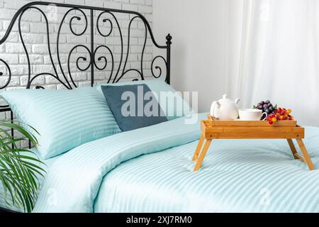 Wooden Breakfast Tray With Teapot, Grapes, and Cup on a Blue Bed Stock Photo