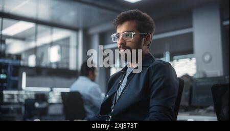 Handsome Indian Software Developer Working on Computer in a Technological Laboratory Environment. Young Man is Thoughtful at His Workplace, Drafting Research Ideas for an AI Development Blockchain Stock Photo
