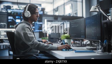 System Administrator Working in a Research E-Business Facility on a Desktop Computer. Focused Software Developer in Casual Clothes Wearing Headphones and Updating Server System Database Stock Photo