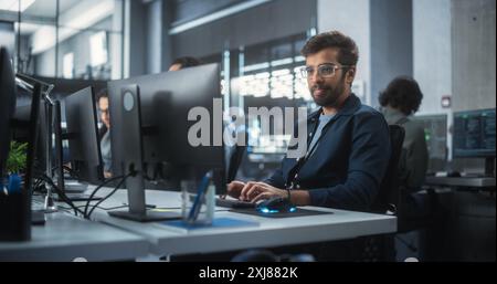 Portrait of a Thoughtful Engineer Working on Desktop Computer in a Technological Office Environment. Research and Development Department Writing Software Code for an Advanced Neural Network Project Stock Photo