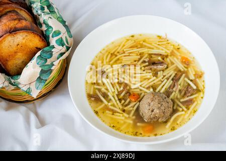 Beef broth soup with noodle, liver dumpling and cerrot soup in white plate, toasted fried bread in basket. Stock Photo
