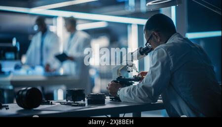 Scientist Using Modern Digital Microscope in a Research and Development Facility. On Blurred Background Diverse Team of Industrial Specialists Working on Remotely Controlled Mobility Robot Stock Photo