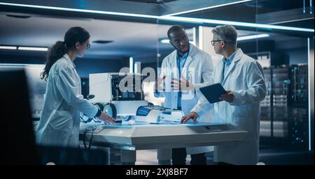 Diverse Team of Industrial Robotics Specialists Gathered Around Table With a Mobile Robot. Engineers In Lab Coats Discussing an Automated Robotic Delivery Assistant with Artificial Intelligence Stock Photo