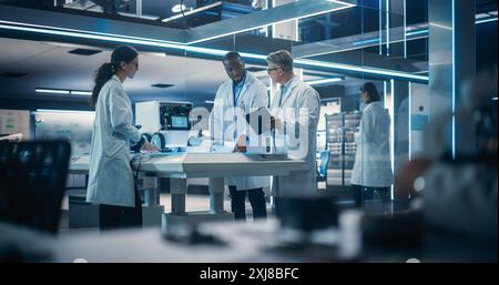 Diverse Team of Industrial Robotics Specialists Gathered Around a Table With a Mobile Robot. Engineers In Lab Coats Discussing an Automated Robotic Delivery Assistant with Artificial Intelligence Stock Photo