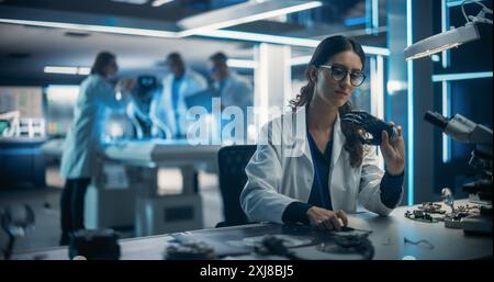 Research and Development Facility with Engineers Working on a High Mobility Robot Dog Project. On Foreground Female Scientist Developing a Prosthetic AI Powered Robotic Hand at Her Desk Stock Photo