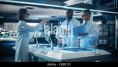 Diverse Team of Industrial Robotics Specialists Gathered Around a Table With a Mobility Robot. Scientist Using Laptop Computer to Program the Automated AI Robotic Dog Stock Photo