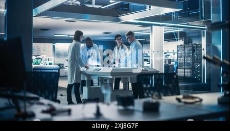 Team of Industrial Engineers Working on a Bionic Robot Arm at a Startup Factory. Multiethnic Male and Female Scientists Having a Conversation About an Electronic Component for a Humanoid AI Robot Stock Photo