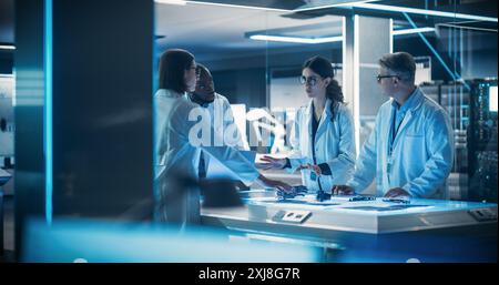 Diverse Team of Industrial Robotics Specialists Gathered Around a Table With Development Parts of a Bionic Robot. Scientist Using Laptop Computer to Test the Prosthetic Hand Prototype Stock Photo