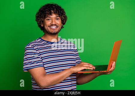 Photo portrait of young senior level programmer indian specialist guy works online using netbook isolated on green color background Stock Photo