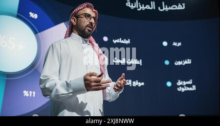 On Business Expo Stage: Famous Inspirational Speaker From Gulf Region Talking about Technology, Science, Success, Productivity. Tech Industry Businessman in Traditional Arab White Clothes Stock Photo
