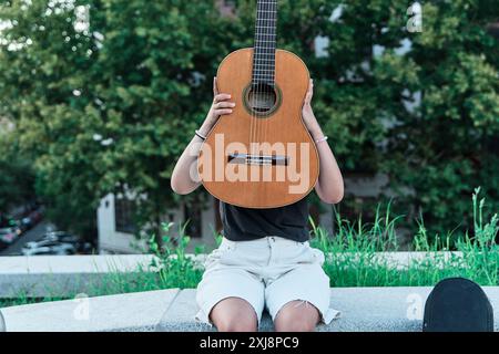 latina woman covering her face with an electric guitar Stock Photo