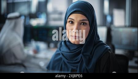 Portrait of a Middle Eastern Female Using Desktop Computer, Looking at Camera and Smiling. Empowered Muslim Information Technology Specialist, Software Engineer, Developer or Data Scientist Stock Photo