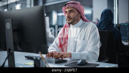 Arab System Administrator Working in a Research E-Business Facility on a Desktop Computer. Focused Middle Eastern Software Developer Updating Server System Database. Gulf Man At Work in Office Stock Photo