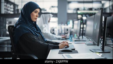 Beautiful Middle Eastern Computer Scientist Wearing a Hijab, Working on PC in a Technological Corporate Office. Young Muslim Woman Writing Software Code for an Innovative Online Service Project Stock Photo