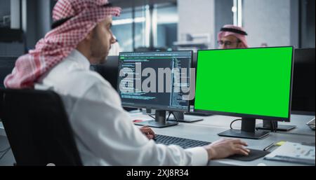 Arab Software Developer Working on Desktop Computer with Green Screen Mock Up Display. Young Middle Eastern Specialist Testing Programming Code for an Innovative Big Data Blockchain Project Stock Photo
