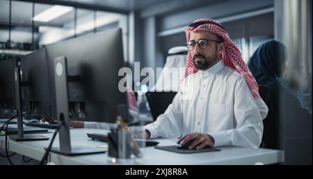 Diverse Young Arab Colleagues Working on Computers in a Research Laboratory. Focus on Muslim Male Software Developer Colleague Working on a Solution for Their Collaborative Industrial Tech Project Stock Photo