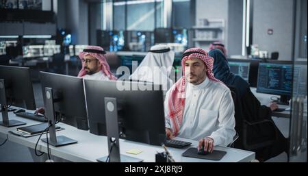Diverse Young Arab Colleagues Working on Computers in a Research Laboratory. Focus on Muslim Male Software Developer Colleague Working on a Solution for Their Collaborative Industrial Tech Project Stock Photo