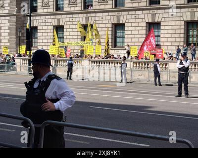 London, UK. 17 July 2024 Onlookers, protestors, and military and police officers line the street of Whitehall leading to the Houses of Parliament in anticipation of the procession which will bring King Charles III to the ceremony of the State Opening of Parliament for the new Labour Government under Keir Starmer.   © Simon King/ Alamy Live News Stock Photo