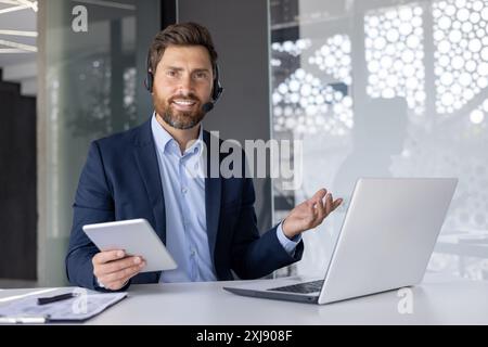 Confident male professional in a smart suit and headset engaging with a client over a video call in a sleek, well-lit office. Stock Photo