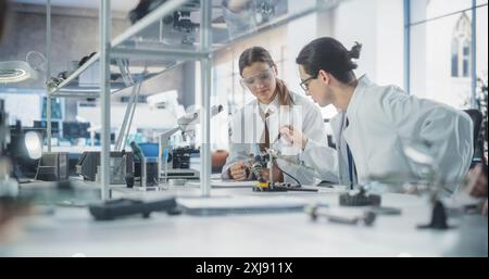 Female and Male Students in Safety Goggles and White Coats Working Together in Science Class, Collaborating on a College Project. Scholars Talking, Study and Prepare for Computer Engineering Exams Stock Photo