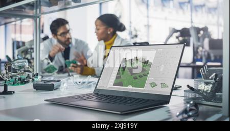 Laptop Computer with Technology Program Display Standing on a Table in a Science Class Laboratory. Diverse Students Practicing Soldering Electronic Components for Their Tech Projects Stock Photo