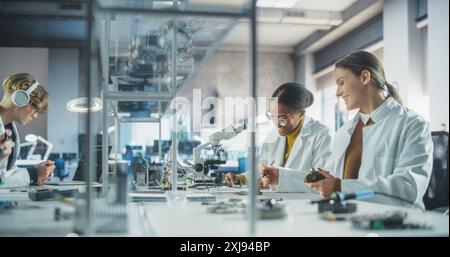 Modern Science Research Laboratory in University: Diverse Young Scientists in White Coats Using Microscopes, Discussing Assignment for a Technology Project in School Stock Photo