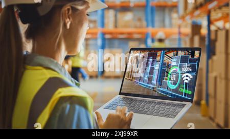 Futuristic Technology Warehouse: Female Worker Doing Inventory, Using Augmented Reality Program On Laptop Computer. Woman Analyzes Digitalized Products Delivery Infographics in Distribution Facility. Stock Photo