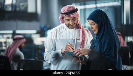 Team of Two Diverse Specialists Use Tablet Computer. Having a Conversation on a Cybersecurity Project. Empowered Young Middle Eastern Male and Female Work on Digital E-Commerce Startup Business Stock Photo