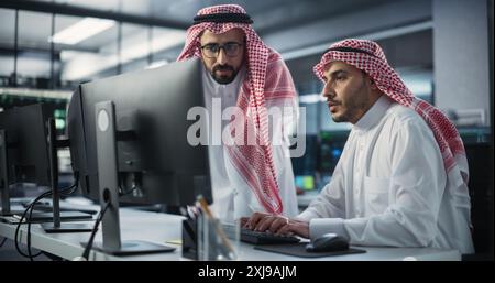 Two Multiethnic Arab Colleagues Having a Conversation While Busy Working on a Software Development Project. Engineer Talking with a Middle Eastern Project Manager. Teamwork in Technology Laboratory Stock Photo