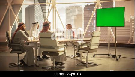Group of Middle Eastern Executives and Management Having Conference Video Call with a Remote International Office. Businessmen Watching a Presentation on TV with Green Screen Mock Up Display. Stock Photo