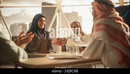 Muslim Businesspeople Closing a Business Deal at a Corporate Modern Office. Female and Male Representatives Shake Hands and Celebrate Successful Partnership. Saudi, Emirati, Arab Office Concept Stock Photo