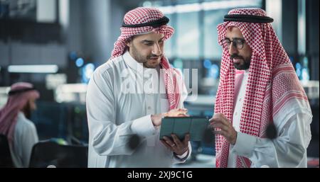 Two Young Muslim Software Engineers Use Tablet Computer to Discuss a Technological Project in a Modern Industrial Office. Arab Scientists Work in Research and Development Center Stock Photo