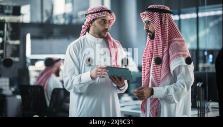 Two Multiethnic Arab Colleagues Having a Conversation While Busy Working on a Software Development Project. Engineer Talking with a Middle Eastern Project Manager, Using Tablet Computer in Office Stock Photo