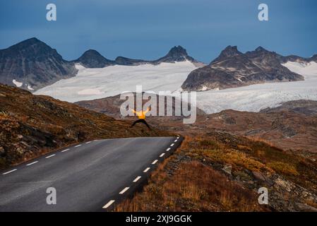 Man in yellow raincoat jumping in front of glacial mountains, Sognefjellet Mountain Pass, Jotunheimen National Park, Norway, Scandinavia, Europe Copyr Stock Photo