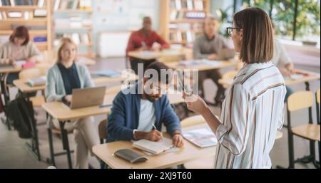 Grown-Up Men and Women Getting Self-Improvement Course in College. Adult Class Writing Down Notes in Notebook and Using Laptop Computers. Tutor Standing in Front of Them and Giving a Lecture Stock Photo