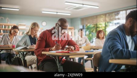 Handsome African Man Writing Down Notes in Notebook. Group of International Mature Students Studying in Classroom. Adult Training Center Help People to Develop New Useful Skills Throughout Life Stock Photo