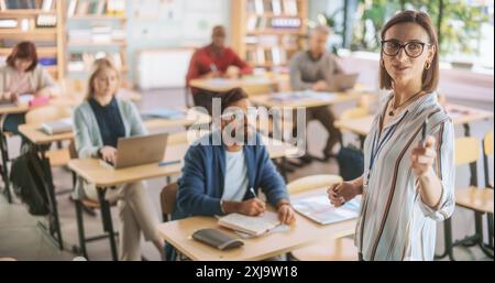 Grown Up Men and Women Getting Self-Improvement Course in College. Adult Class Writing Down Notes in Notebook and Using Laptop Computers. Tutor Standing in Front of Them and Giving a Lecture Stock Photo