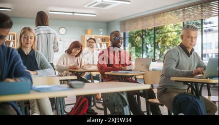 Adult Education Center: Diverse Mature Students Learning in Classroom, Using Laptop Computers and Writing in Notebooks. Group of People Taking a Workshop on Improving Professional Work Skills Stock Photo