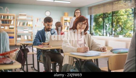Diverse Mature Students Learning in Classroom, Using Laptops and Writing in Notebooks. Senior Female Motivated to Learn New Skills During Adult Education Course in School, Completing An Assignment. Stock Photo