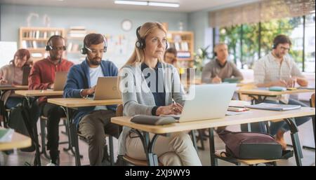 Grown Up Men and Women Getting a Remote Audio Course in College. Adult Class Writing Down Notes in Notebook and Using Laptop Computers. Teacher Giving Lecture Remotely from Home Stock Photo
