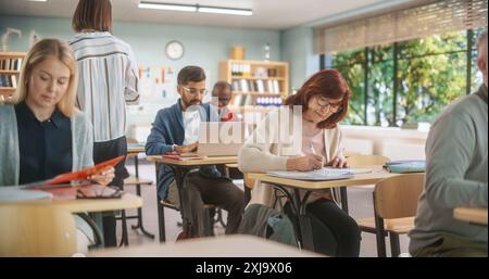 Diverse Mature Students Learning in Classroom, Using Laptops and Writing in Notebooks. Senior Female Motivated to Learn New Skills During an Adult Education Course in School, Completing An Assignment. Stock Photo