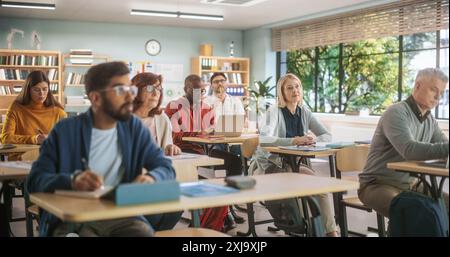 Diverse Mature Students Learning in Classroom, Using Laptops and Writing in Notebooks. Male And Female Class Attendees Listening to Lecture And Taking Notes During Adult Education Course in School Stock Photo