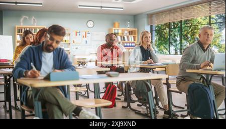 Diverse Mature Students Learning in Classroom, Using Laptops and Writing in Notebooks. Male And Female Class Attendees Listening to Lecture And Taking Notes During an Adult Education Course in School Stock Photo